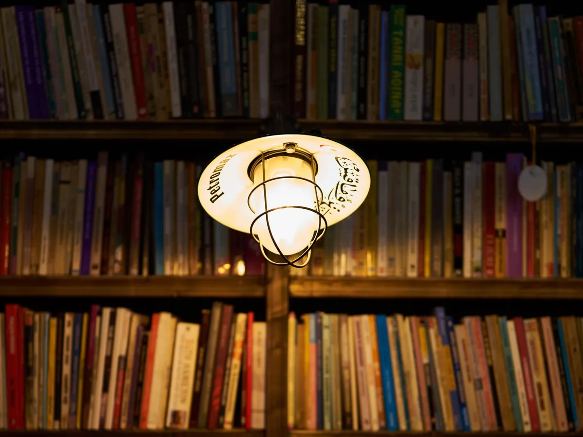 A wall of bookshelves lit by a warm hanging lamp